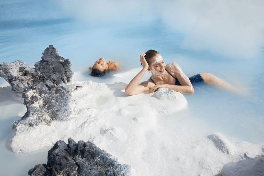 Two women at the Blue lagoon relaxing on a rock with facemasks