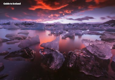 Jokulsarlon glacier lagoon looks extra magical under a dark cloudy sky with vibrant shades of red lighting the sky and water.