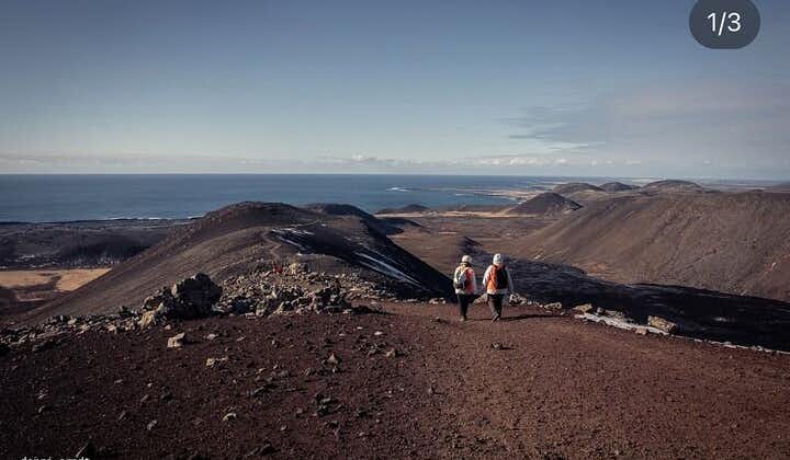 People walk along stark and hilly volcanic terrain on the Reykjanes Peninsula with the sea beyond.
