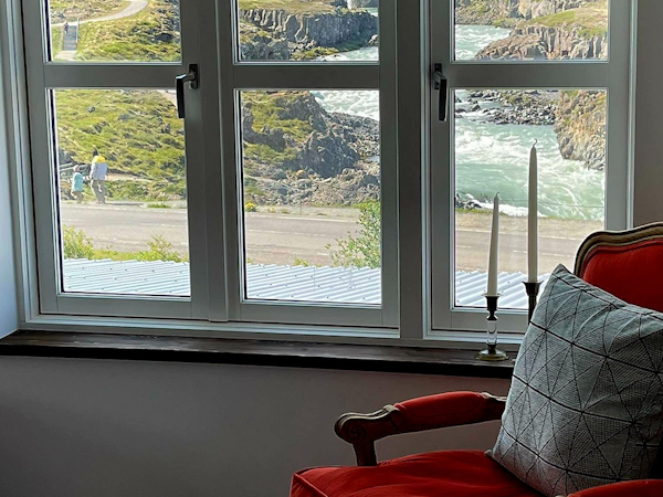 An armchair by a window with gorgeous river and waterfall views at Hotel Godafoss.