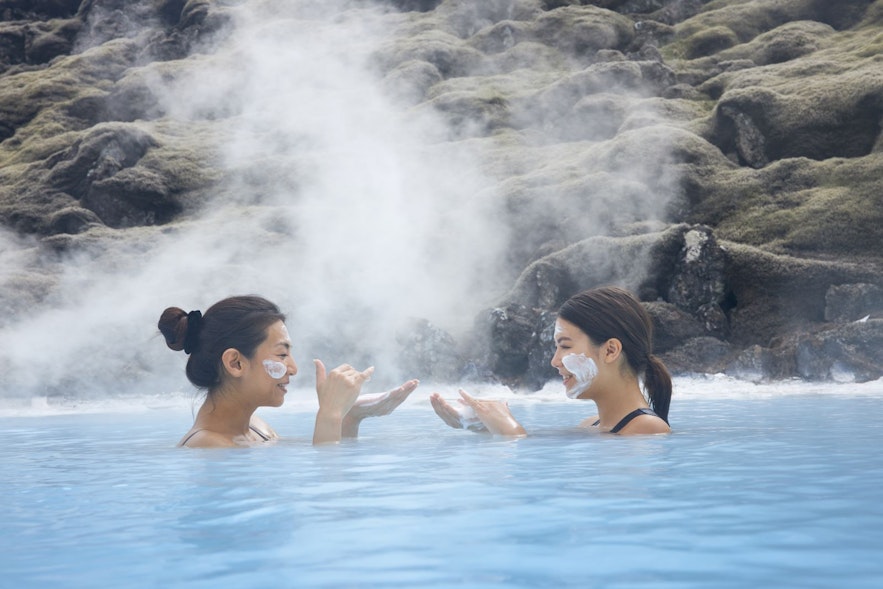 Two women enjoying face masks at the blue lagoon in Iceland with moss in the backgound