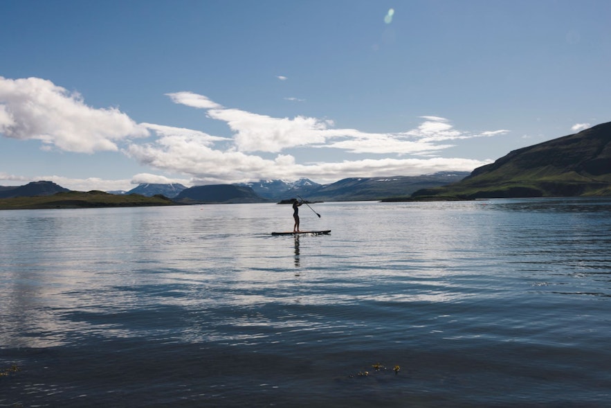 Person paddle boarding at Hvammsvik Hot Springs with beautiful Hvalfjodrur in the background