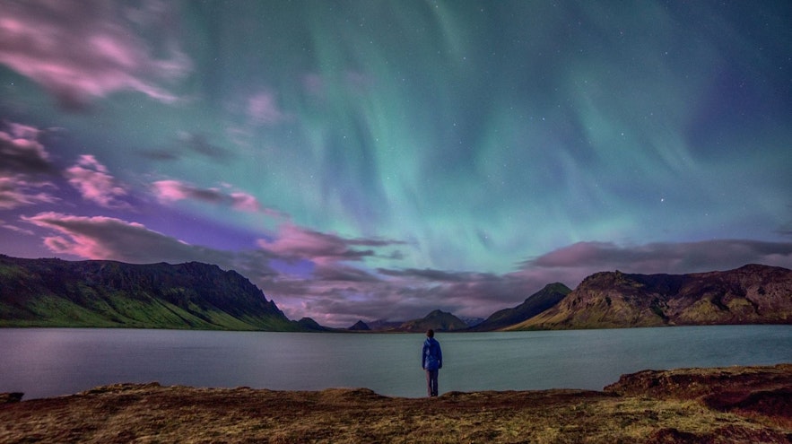 游客站在冰岛湖边观赏极光