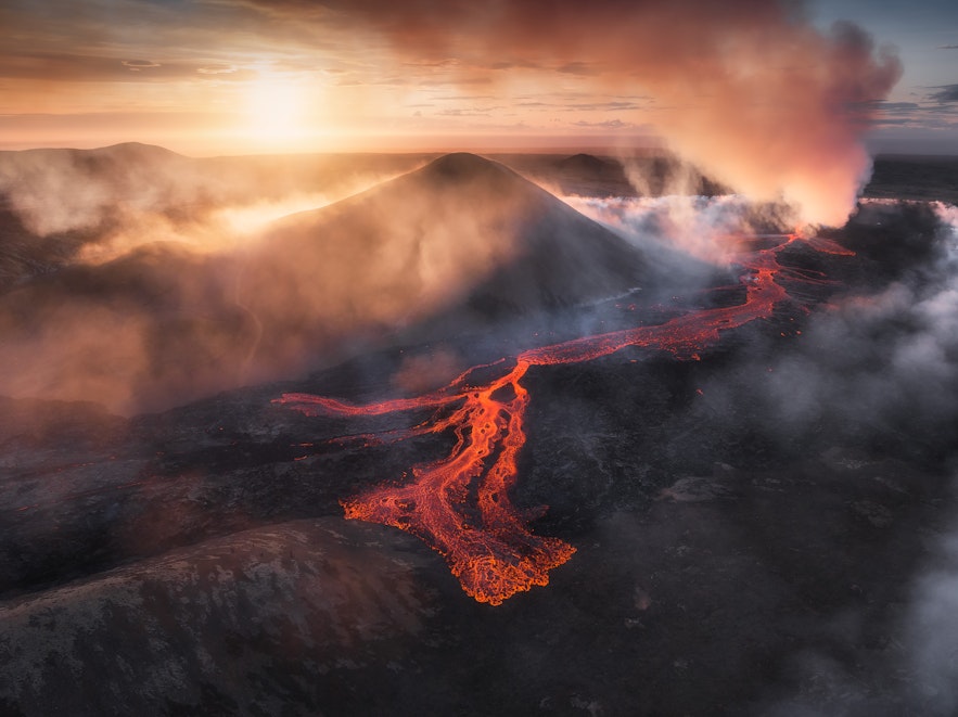Из активного вулкана 2023 года вытекает лава, и газ разносится над местностью вокруг извержения вулкана Литли-Хрутур на фоне заката на полуострове Рейкьянес в Исландии