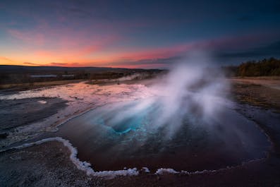The Geysir geothermal area is an otherworldly landscapes of steaming fumaroles, boiling mud pits, and exploding geysers, an incredible sight under Iceland's colorful winter night sky.