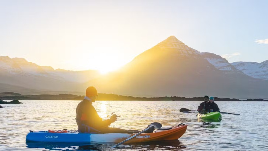 People kayaking on the Berufjordur fjord in east Iceland with the sun setting over the mountains by Djupivogur