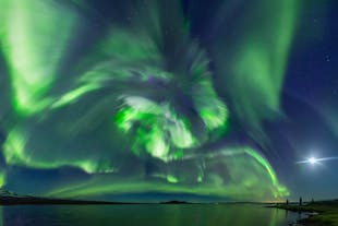 A swirl of aurora borealis illuminating a coastline in Iceland.
