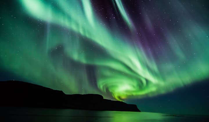 The northern lights swirl in brilliant colors of green and purple in the winter night sky.