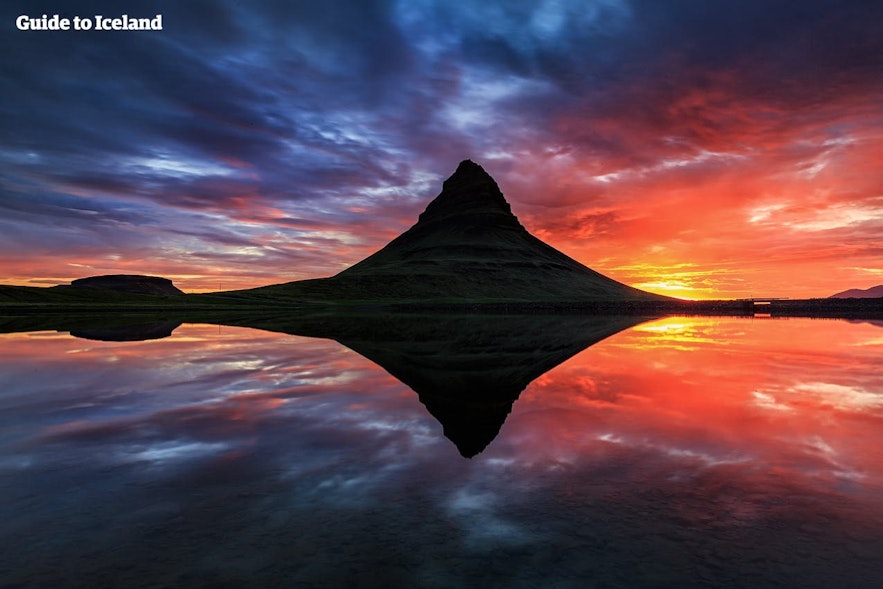 Der Berg Kirkjufell auf der Halbinsel Snaefellsnes spiegelt sich unter der Mitternachtssonne auf der ruhigen Wasseroberfläche.