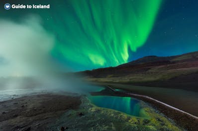 The northern lights shining over the Geysir geothermal area in winter in Iceland.