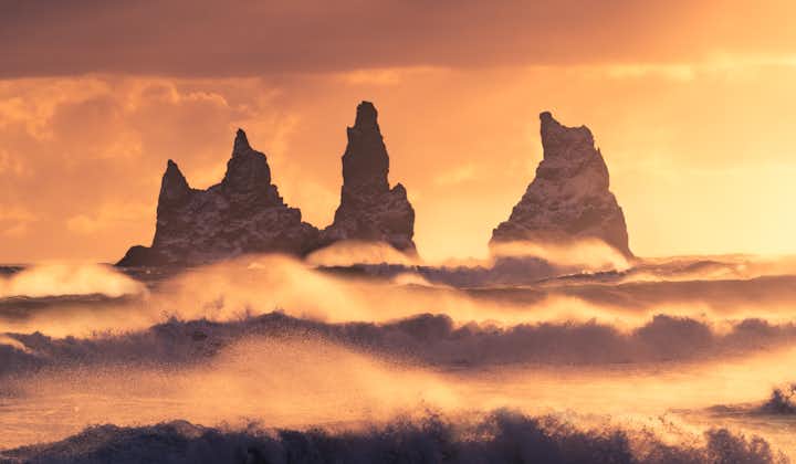 Die Reynisfjara-Meeresstapel bilden bei Sonnenuntergang eindrucksvolle Silhouetten vor dem farbenprächtigen Himmel.