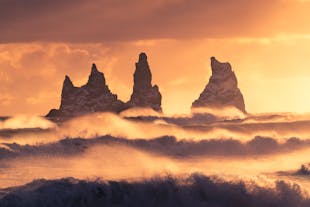 Reynisfjaras fjelltopper danner slående silhuetter mot den fargerike himmelen i solnedgangen.