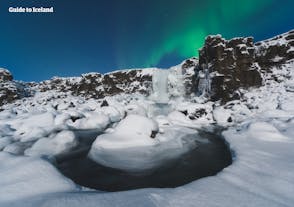 La cascata Oxararfoss, nel parco nazionale Thingvellir, è meravigliosa, circondata da un paesaggio innevato con l'aurora boreale sullo sfondo.