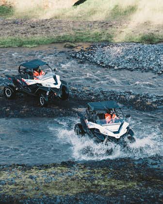 Two people driving buggies through a river near the Myrdalsjokull glacier in South Iceland.