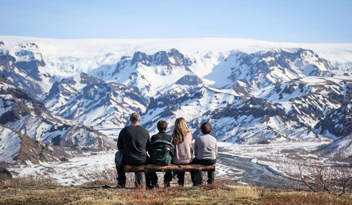 A family of four sits on a bench overlooking the snowy mountains of the Thorsmork Valley.