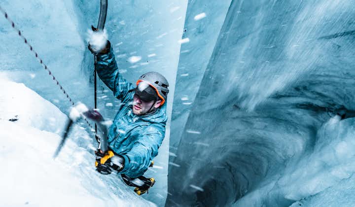 A person ice climbing in a deep crevice with ice from the wall sprinkling over them and into the crevice's depths.