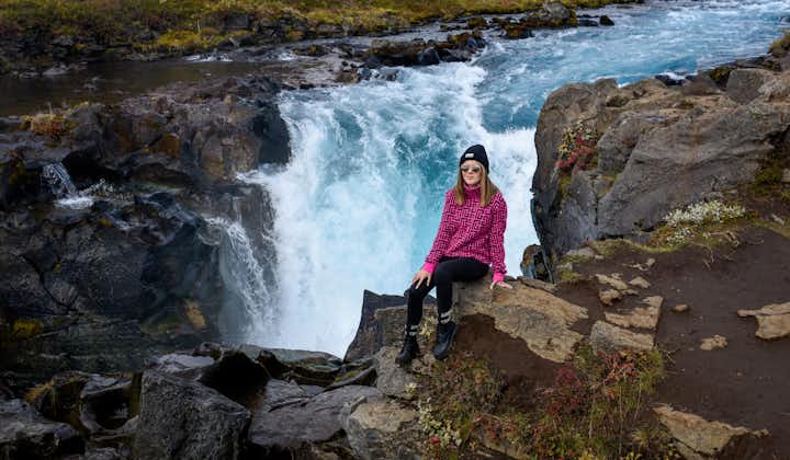 A photo of a traveler posing in front of the Bruarfoss waterfall in Iceland.