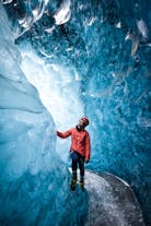 A person in a red coat and helmet poses for a photo inside an ice cave.