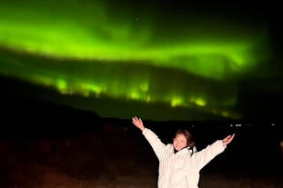 A person stretches their arms out wide with the aurora borealis lighting up the sky overhead.