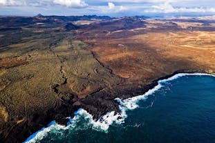 An aerial view over lava fields down to the coastline on a helicopter volcano tour.