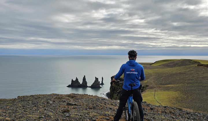 A cyclist stops to enjoy gorgeous views of the Reynisdrangar sea stacks and the Atlantic Ocean from the Reynisfjall peak.