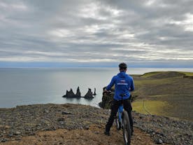 A cyclist stops to enjoy gorgeous views of the Reynisdrangar sea stacks and the Atlantic Ocean from the Reynisfjall peak.
