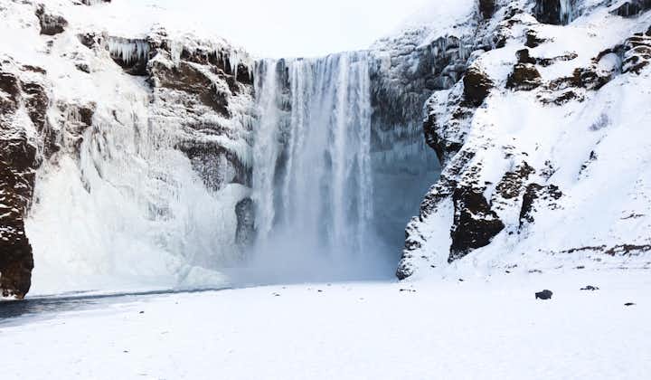 Capture the surreal beauty of Skogafoss in winter's grip, as the waterfall's powerful flow is partially frozen.