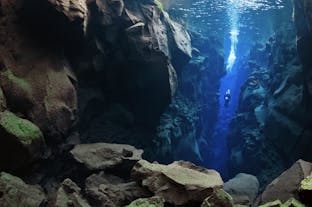 A diver explores a narrow part of the Silfra fissure amid a fascinating, rocky underwater landscape and vibrant colors.