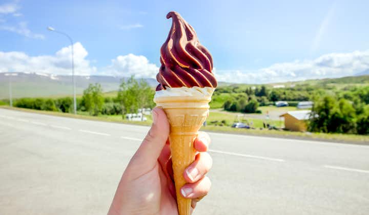 Hand holding tasty Icelandic local soft serve vanilla ice cream dipped in hot chocolate, with Iceland nature in the background.