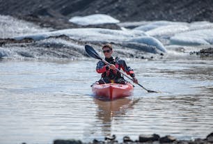 A person kayaks on the tranquil waters of the Solheimajokull glacier lagoon.