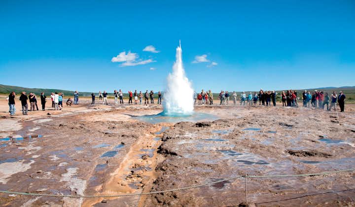 People watch as the Strokkur geyser erupts high in the air at the Geysir geothermal area in the Haukadalur valley.