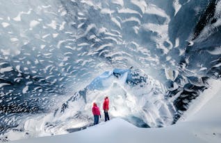 Two travelers in red puffer coats stand in an ice cave beneath the Myrdalsjokull glacier.