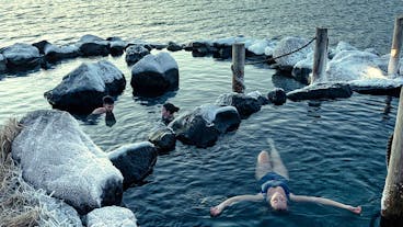 A person floats on their back, relaxing in one of the natural hot pools at the Hvammsvik Hot Springs.