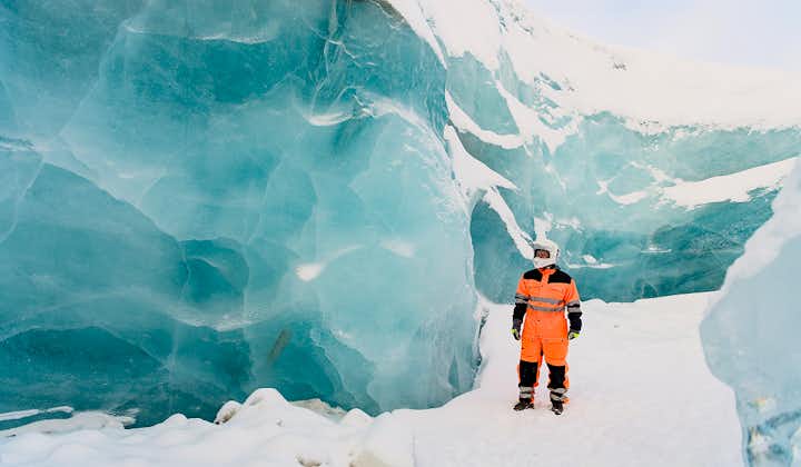 A person wearing a snowmobiling suit and helmet stands on the Langjokull glacier next to a massive ice wall.
