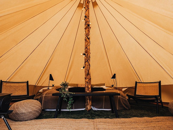 The inside of one of the Golden Circle Tents, with a double bed with blankets, a large beam holding up the structure, and chairs