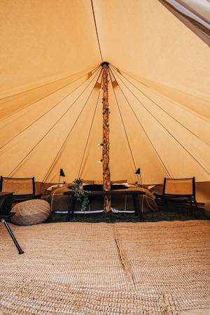 The inside of one of the Golden Circle Tents, with a double bed with blankets, a large beam holding up the structure, and chairs