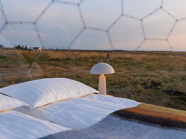 An interior view of an Aurora Igloo glamping pod, showing the bed and a bedside lamp.