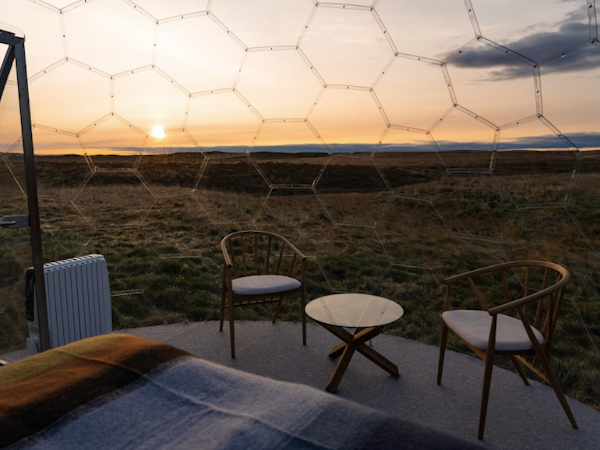 A small table and two chairs inside an Aurora Igloo pod, with a sunset in the background outside.