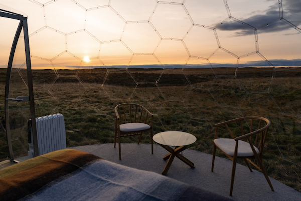 A small table and two chairs inside an Aurora Igloo pod, with a sunset in the background outside.