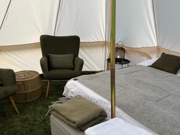 The interior of a glamping tent at Golden Circle Tents with a bed, ottoman, towels, and a chair.