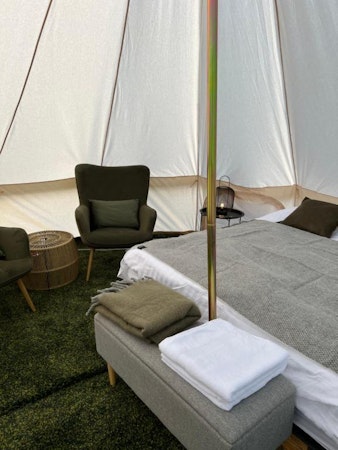 The interior of a glamping tent at Golden Circle Tents with a bed, ottoman, towels, and a chair.
