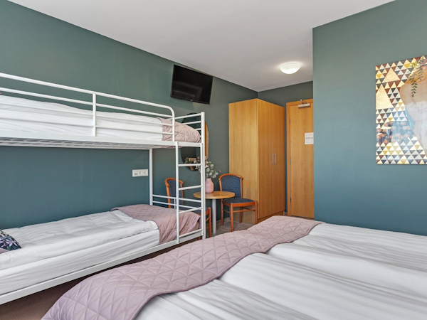 The family rooms at Hotel Kvika have a double bed, bunk beds, a table, chair, and closet.