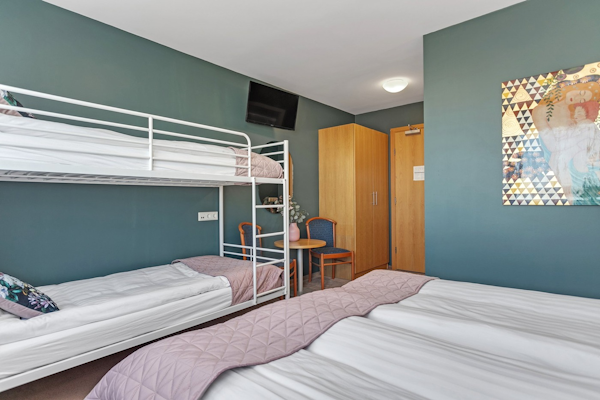 The family rooms at Hotel Kvika have a double bed, bunk beds, a table, chair, and closet.