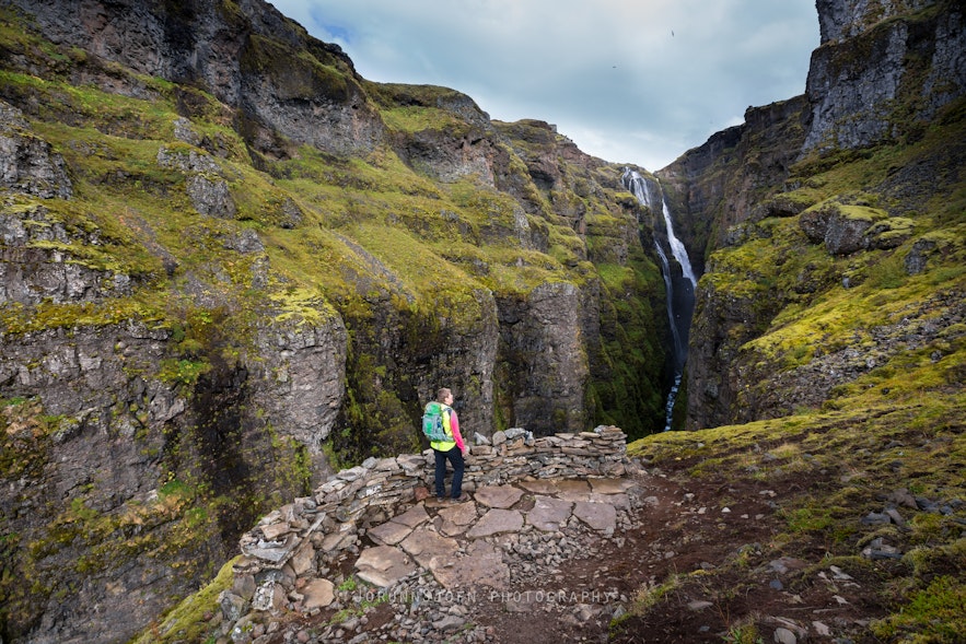 Person standing staring at Glymur waterfall in the distance