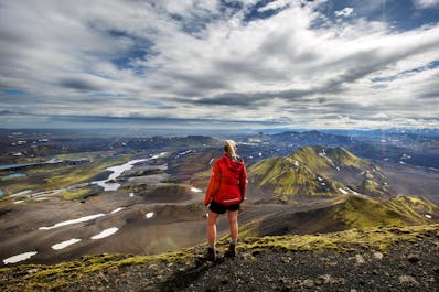 A person stands on a peak overlooking the incredible mountain scenery of the Icelandic Highlands.