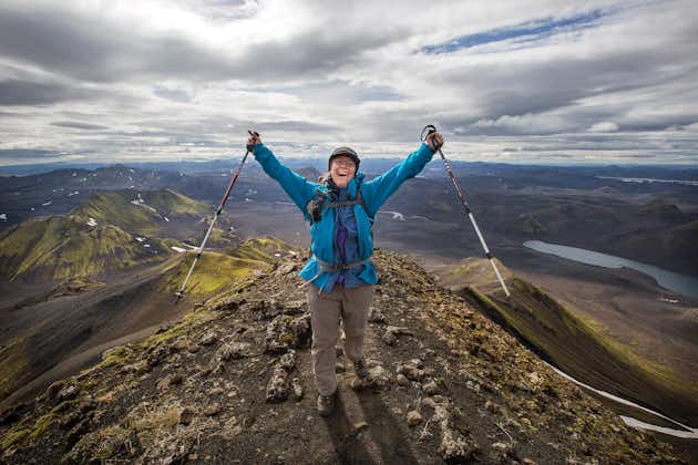 A hiker raises her arms and hiking poles in the air on a mountain in the Icelandic Highlands.