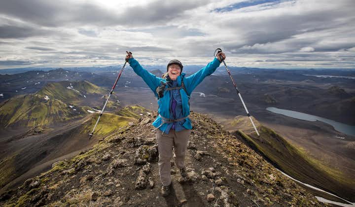 A hiker raises her arms and hiking poles in the air on a mountain in the Icelandic Highlands.