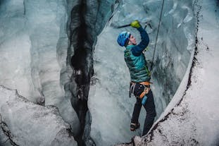A person climbs up a wall of ice on an ice climbing tour in Iceland.
