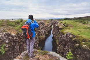 A person takes a photo from a rugged outcrop of a pristine water-filled fissure in the Thingvellir National Park.