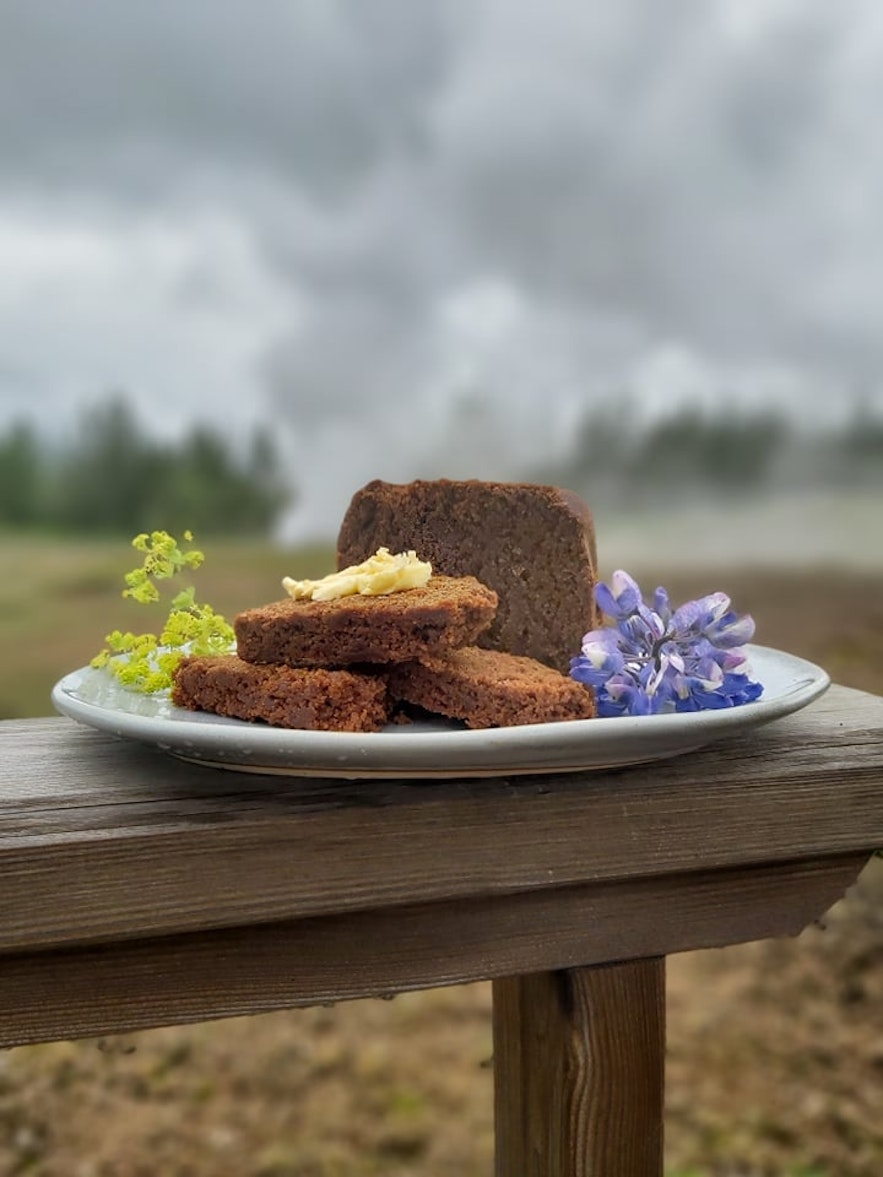 Homemade rye bread and butter on a plate, with steam rising from the ground above in the background.
